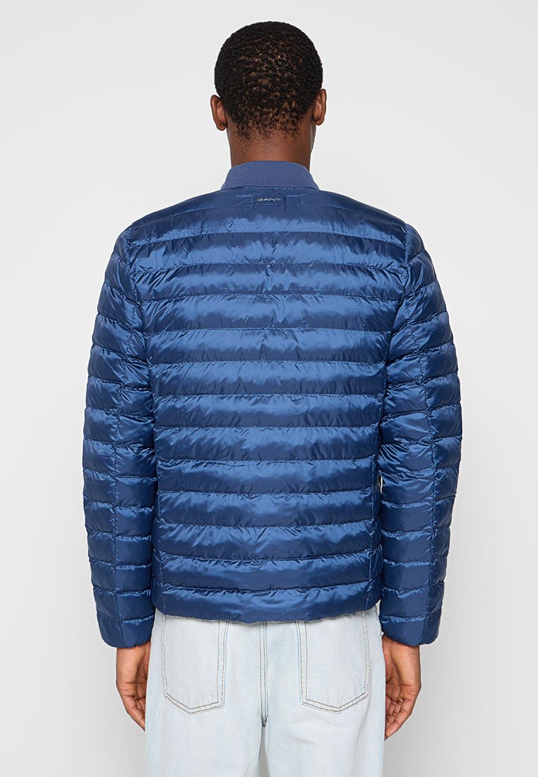 Granatowa kurtka puchowa z pikowanym wzorem, błyszczącą teksturą i stojącym kołnierzem. Widoczne logo z tyłu w okolicy szyi.