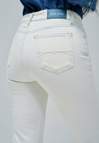 Jeans salsa blancos con diseño ajustado, que cuentan con dos bolsillos traseros con detalles de costura y una etiqueta de marca azul situada por encima de la cinturilla.