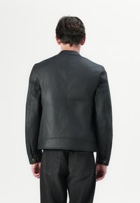 Jachetă din piele neagră, cu o croială ajustată, având o textură netedă și umeri structurați, asortată cu blugi de denim închisi la culoare.