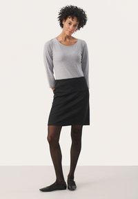 Haut à manches longues gris associé à une jupe à carreaux noirs. La tenue présente une coupe ajustée et est complétée par des collants foncés et des ballerines noires.