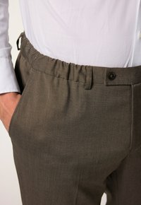 Hosen mit elastischem Bund aus braunem Stoff, mit Knopfverschluss, seitlichen Taschen und strukturierter Oberfläche.