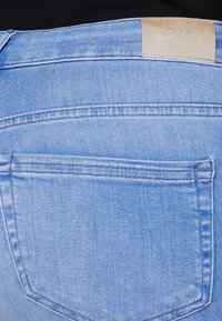 Ljusblå denimjeans med en enda bakficka och en läderetikett, med stickade detaljer och en jämn yta.