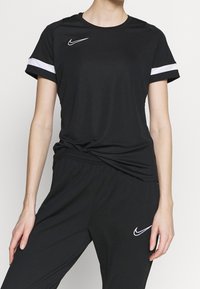 Svart idrottströja med korta ärmar, vita detaljer på ärmarna, rund halsringning och Nike-logotyp på bröstet. Matcher med svarta byxor som passar.