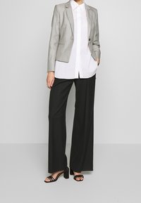 Blazer gris avec un design ajusté, un bouton unique et des revers crantés sur une chemise blanche à boutons. Associé à un pantalon noir à jambes larges et des sandales à lanières.