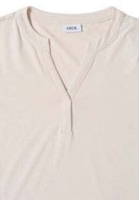 Top beige a maniche corte con scollo a V, realizzato in tessuto morbido, dotato di una piccola chiusura e dell'etichetta del marchio "CECIL" sul colletto.