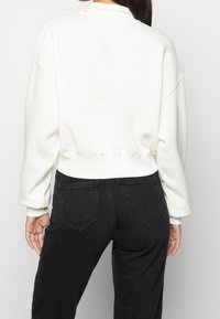 White cropped sweatshirt with a round neckline and dropped shoulders, paired with black jeans featuring back pockets. Smooth texture.