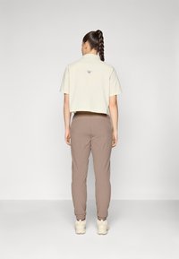 Bordeaux kleurige cropped lichtbeige shirt met een kraag en logo op de achterkant, gecombineerd met slanke bruine broek en beige sneakers. Eenvoudig en functioneel ontwerp.