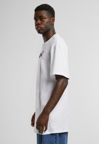 White cotton t-shirt with a round neck, short sleeves, and a graphic print on the chest, paired with blue denim jeans. Simple design.