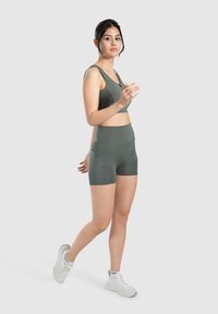 Zelená sportovní podprsenka a šortky s vysokým pasem s hladkým povrchem, které mají přiléhavý střih a kontrastní šití, doplněné bílými teniskami.