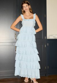 Rochie fără mâneci, cu un nuanță deschisă de albastru, cu volane, bretele cu pliuri, margini din dantelă perforată și o siluetă fluidă. Purtați-o cu sandale cu toc în culori deschise.