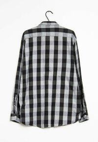 Camicia a maniche lunghe a scacchi nera e grigia con colletto, dotata di polsino con bottone, appesa a un gancio nero su uno sfondo bianco.