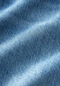 Gros plan d'un tissu en denim bleu montrant une texture de tissage détaillée et de légères plis avec des ombres variées.