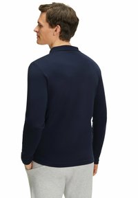 Dunkelblauses langärmliges Poloshirt mit klassischem Kragen, glatter Textur, minimalem Branding und taillierter Passform, kombiniert mit hellgrauen Hosen.
