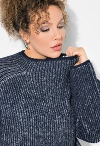 Marineblauer, gerippter Strickpullover mit hohem Kragen und weiten Bündchen, hergestellt aus einem strukturierten Garn für Wärme und Komfort.