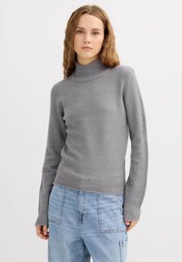 Suéter de cuello alto gris con dobladillo y puños acanalados, hecho de tela suave. Combinado con jeans azul claro de corte holgado.