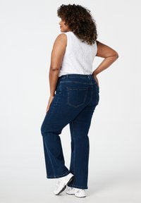 Donkerblauwe denim jeans met een recht gesneden pijp, voorzien van achterzakken en een hoge taille. Gepaard met een witte mouwloze top.