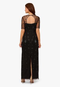 Schwarzes Abendkleid mit durchsichtigen kurzen Ärmeln, verziert mit silberner Perlenstickerei in Blumenmustern, mit einem Rückenschlitz und einem Schlitz bis zur Kniehöhe.