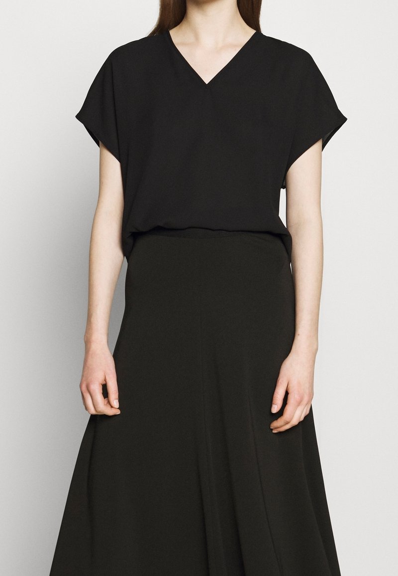 Haut noir à manches courtes avec un col en V et une coupe ample, associé à une longue jupe noire, créant un look monochrome et une texture lisse.