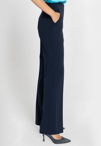 Granatowe spodnie o prostym kroju, z bocznymi kieszeniami i gładką teksturą materiału, połączone z szarymi czółenkami w szpic.