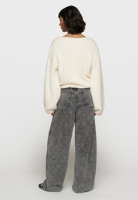 Suéter de punto crema con mangas oversize combinado con jeans de pierna ancha grises que presentan un sutil patrón en toda la prenda y detalles de costura en contraste.