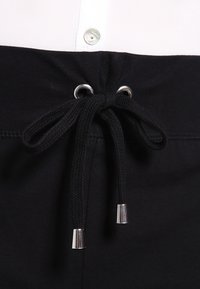 Svarta sweatpants med dragsko i midjan, försedd med silverfärgade metalldelar och öglor. Slät yta med en åtsittande passform.