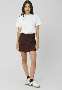 T-shirt en coton blanc avec le texte "please" ; jupe portefeuille en tweed bordeaux avec un motif texturé. Le modèle porte des baskets blanches et marron.