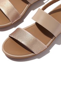 Beige Sandalen mit zwei breiten Riemen; ein Riemen aus glattem Leder, der andere mit einem metallischen, durchbrochenen Design. Braune Innensohle, Gummisohle.
