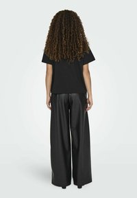 Camisa negra de manga corta combinada con pantalones de imitación cuero negros de corte holgado, con una textura suave y piernas anchas. Vista trasera mostrada.