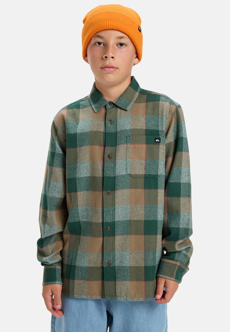 Groene en beige geruite flanellen shirt met lange mouwen, knoopsluiting aan de voorkant, een enkele borstzak en een klein zwart logo patch. Oranje gebreide beanie.