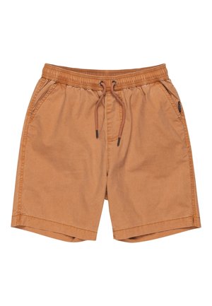 Chłopiec ubrany w jasnoniebieską koszulkę z nadrukiem „Skull Island”, brązowe szorty, czarne skarpetki oraz czarne trampki z białymi sznurowadłami.