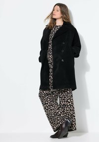 Černý, sametový, dvouřadý kabát s velkými knoflíky, vrstvený přes béžové šaty a široké leopardí kalhoty, doplněný o boty na podpatku.