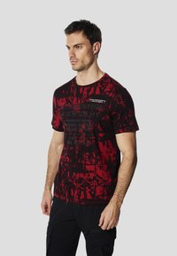 Grafické tričko v černé a červené barvě s abstraktním potiskem, krátkými rukávy, kulatým výstřihem a textovým detailem uprostřed. Bavlněný materiál.