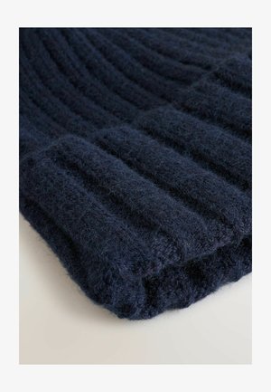 Tumesinine kudumüts, millel on sooniline tekstuur. Valmistatud pehmest ja kohevast lõngast, omab see voltimist ja sujuvat, ümarat kuju.