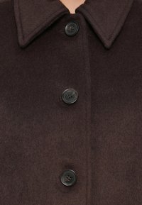 Abrigo de mezcla de lana marrón oscuro con cuello de muesca, cinco botones y una textura suave. Presenta un diseño elegante y aerodinámico.