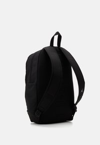 Mochila negra con correas de hombro acolchadas, compartimentos con cremallera y una marca sutil. Hecha de un tejido texturizado con una forma estructurada.