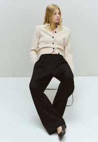 Cárdigan de punto beige con botones negros sobre pantalones de pierna ancha negros. El conjunto presenta materiales texturizados y un corte relajado.