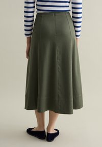 Olive green A-line skirt with a smooth texture, featuring a mid-calf length and back pleat detail. Worn with dark blue slippers.