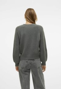 Maglione grigio lavorato a maglia con dettaglio a coste sulle maniche, scollo rotondo e fit cropped, abbinato a jeans grigi a vita alta.