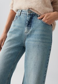 Lichtblauwe spijkerbroek met een hoge taille, voorzien van een metalen knoopsluiting, vijf zakken en subtiele vervaging op de stof.
