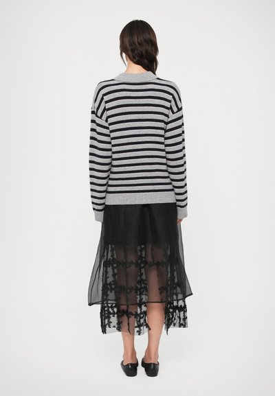 Röstripeeritud hall ja tumesinine sviiter, mis on kombineeritud läbipaistva musta seeliku ja lillekirjaga hemist. Lihtsad mustad korterjalatsid täiendavad välimust.