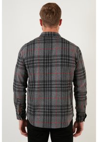 Camicia a quadretti grigia con accenti rossi, maniche lunghe, polsini con bottoni e orlo arrotondato. Il tessuto appare texture e leggermente pesante.