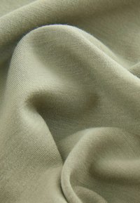 Mäkká, ľahká tkanina v jemnej olivovo zelenej farbe so hladkým povrchom; má jemne rebrovaný vzor a mierne priesvitnosť.