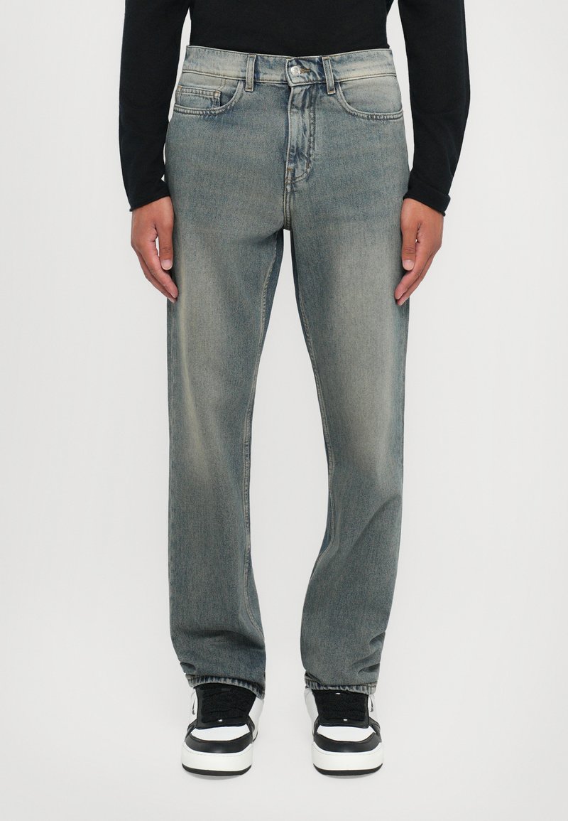 Light gray denim jeans with a straight-leg cut, featuring a faded finish and classic five-pocket design. Worn with black and white sneakers.