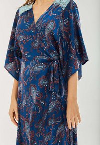 Navy wrap dress in lightweight fabric featuring paisley patterns in blue and red, with a lace trim around the neckline and loose sleeves.