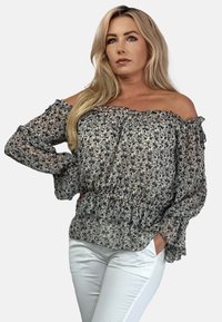 Kwiatowa bluzka bez ramiączek z lekkiego materiału, z falbaniastymi brzegami i elastycznym paskiem w talii, w ciemnoniebieskie i białe wzory. Stylizowana z białymi spodniami.