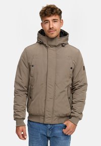 Khaki pufferjakke med justerbar hætte, frontlommer og ribbede manchetter. Har diskrete stikninger og en varm, isoleret tekstur.