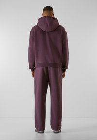 Haut à capuche violet et pantalon de survêtement assorti en tissu doux, présentant une coupe décontractée et des poignets côtelés. Coutures visibles et accent de capuche.
