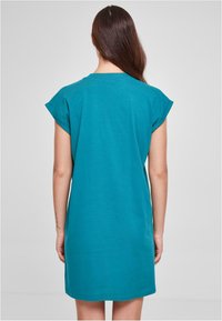 Robe en coton teal avec des manches courtes retroussées, un col rond et une coupe relaxée, tombant au-dessus des genoux. Design simple et uni.