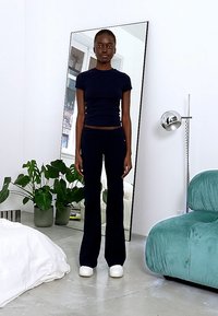 Marineblauw tweedelig outfit met een aansluitend top met korte mouwen en wijde broek, gemaakt van een gladde stof. Model staat naast een spiegel.