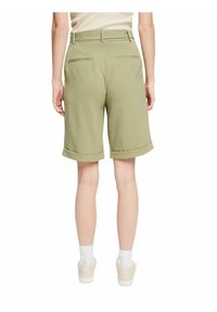 Shorts en coton verts avec un ourlet retroussé, deux poches arrière et une coupe droite, associés à des chaussettes blanches et des chaussures claires.